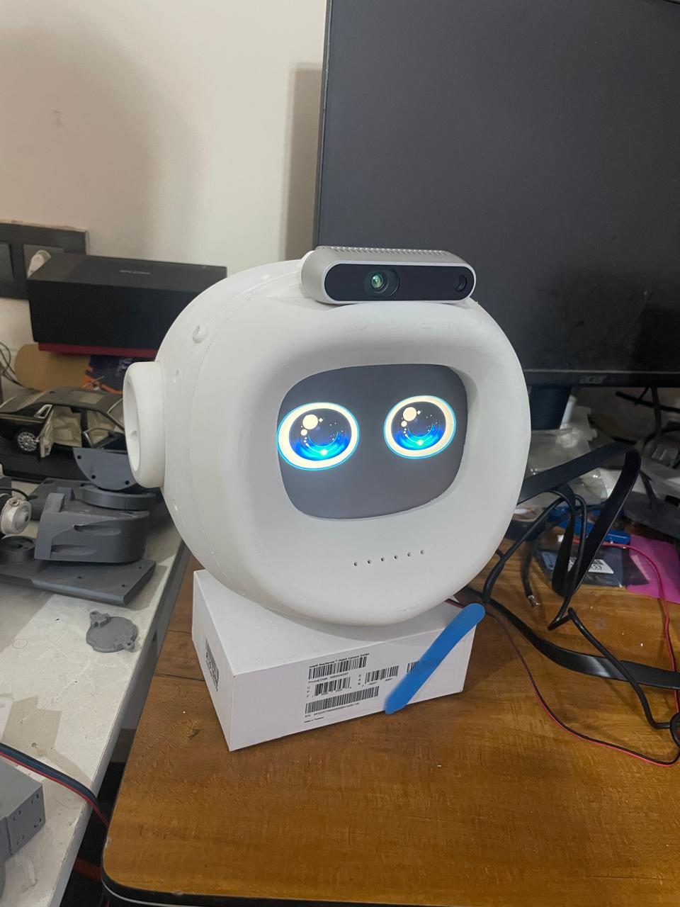 Origin's head with a display face showing blue animated eyes and a depth camera on top